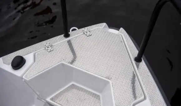 White boat deck showing textured flooring and two black handrails, with dark water in the background.